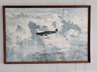 Full front view of wood framed print 'The Lone Spitfire' showing the airplane flying in clouded sky, signed by Gerald Coulson.