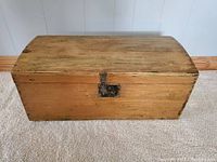 Front view of vintage wooden toolbox showing the curved lid and metal latch with keyhole.