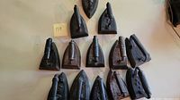 Top-down view of 13 antique cast flat irons arranged on a table showing their various sizes and handle designs.
