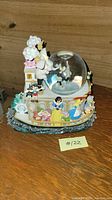 Front and left side view showing the Disney music box with Snow White, Seven Dwarfs, Pinocchio, and Alice figurines around the base and Mickey Mouse in the snow globe.