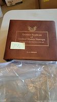 Front cover of brown leather-bound book with gold embossed title 'Golden Replicas of United States Stamps by M. M. Stewart'