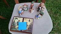 Top-down photo showing six figurines and closed wooden bi-fold box with Norman Rockwell artwork on two panels.
