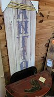 Photo showing partial view of vertical rustic wooden sign with large 'ANTIQUES' text in purple and thick rope accent on top, alongside black metal table with reddish wooden top showing boot and star design.