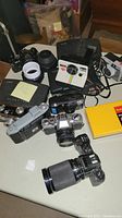 Photo showing multiple vintage Polaroid and film cameras including lenses and cases on table.
