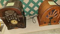 Photo of two vintage cathedral style radios placed side by side on a shelf, showing their overall design and wood cabinetry.