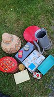 Wide shot showing the entire assortment of vintage tins, woven basket, metal canister with hose, turquoise tray, small boxes, and napkins on grass