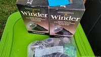 Two wristwatch winders in original packaging displayed on a green surface