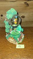 Photo of the snow globe showing Winnie The Pooh inside the globe, with a tree and detailed base including characters and surrounding landscape.