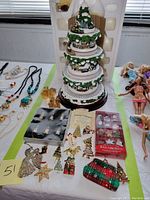 Full view of multi-tier Thomas Kinkade animated Christmas tree surrounded by assorted Christmas jewelry brooches and boxed glass ornaments.