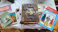 Photo of the entire lot showing the antique Bible, several vintage books on birds, gardening, paper dolls, and a wooden wind chime on a white cloth.