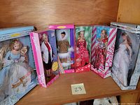 Photo showing all six boxed Barbie dolls arranged side by side on a wooden shelf