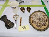 Lot arranged on display surface showing all items together: Belleek vase, brass hand wall hooks, scissors with brass cameo case, and fabric trivet.