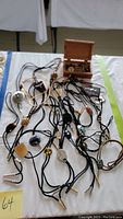 Photo showing multiple bolo ties with different slide decorations and accessories including wooden pipe, business card holder, and money clip arranged on a white cloth.