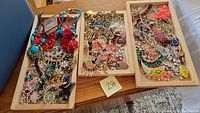 Full overview of three trays filled with a wide assortment of colorful costume jewelry including rhinestone necklaces, pins, brooches, and earrings.