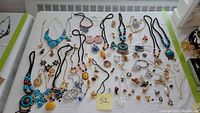 Overview photo of the full assortment of costume jewelry laid on a white surface showing necklaces, bracelets, pins, and earrings with bright colors including blue, black, gold, red, and yellow.