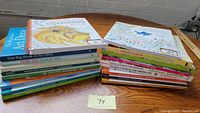 Photo showing two stacks of grown-up coloring books on a wooden surface against a brick wall background. Various titles and themes are visible.