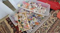 Three plastic bins filled with assorted beads and jewelry making supplies placed on a patterned carpet.