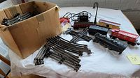 Overview of box with many metal track pieces, train cars, and accessories.
