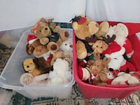 Two plastic bins containing multiple plush animals including teddy bears, moose, dogs, Santa dolls, and a porcelain baby doll with one missing eye.