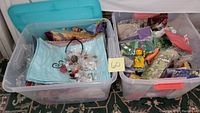 Two plastic bins filled with scarf, costume jewelry, and fabric jewelry bags including blue pashminas and patterned silk scarves.