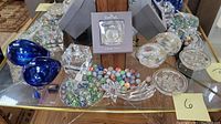 Overview of lot including Swarovski boxed ornament, blue blown glass pieces, various marbles, and clear glass pieces on mirrored shelf.