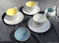 Set of three cups and saucers with cream jug and sugar bowl on grey background showing ribbed design and pastel interiors