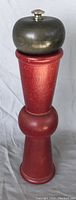 Full view of the red wooden Memphis style pepper grinder with dark wood top and silver knob.