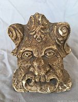 Front view of ceramic gargoyle sculpture showing detailed facial features and ornamental curls.