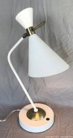 White metal desk lamp with dual conical shades and brass accents on a round base, photographed from front angle.