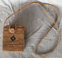 Full front view of woven basketry purse showing geometric pattern, flap with button closure, and long braided strap.