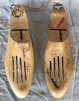 Pair of wooden shoe forms made from cedar with metal iron rings at the heel. Both embossed with size 5D and marked with handwritten notes and some stains.