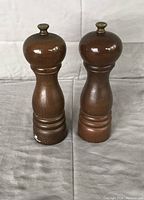 Front view of the two wooden salt and pepper grinders showing their polished brown wood and shape.