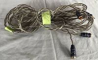 Two long twisted clear-sheathed speaker cables coiled and laid flat with black connectors on both ends; two connectors need replacement.