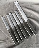 Photo showing six Sabatier knives laid out, five smaller and one larger with protective blade covers.