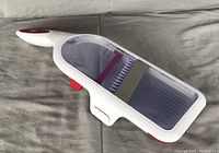 Full side view of the mandoline slicer showing the white and red plastic handle, transparent container, and blades.