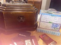 Photo showing two decorative boxes, one wood with bronze fixtures and one floral-patterned cardboard box with drawers, plus multiple lighters in front.