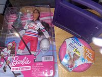 Barbie doll in hockey outfit with accessories in packaging, Aqua Mini Disc float, and purple iPad case shown together on wooden surface