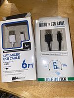 Photo showing front of packaging of two micro USB cables, one white by Mobile Essentials and one black by INFINITEK, both 6 ft long