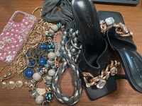 Black heeled sandals with gold chain and clear gems shown with various jewelry and an iPhone case on table