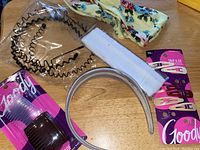 Photo showing assortment of hair accessories including floral fabric headband, white elastic headband, zig-zag plastic headbands, snap clips, and combs.
