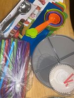 Photo showing metal cream scoop, plastic measuring cups, colorful straws, silicone baking mats, and gray divided tray.