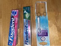 Photo of two Fixodent denture adhesive tubes and one sealed Oral-B EasyFlex toothbrush replacement head.
