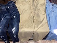 Three pairs of pants laid flat: two pairs of distressed blue denim jeans and one pair of khaki work pants.