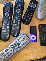 Photo showing five remote controls, a purple Apple iPod Nano, and a black Uniden cordless phone handset on a table.