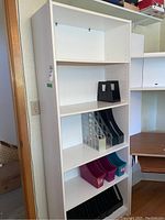 Full view of tall white bookcase with four shelves containing multiple plastic book/file organizers in black, grey, pink and teal.