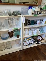 Photo showing two white bookcases filled with various glassware, mugs, containers and decorative items for size reference, contents not included.