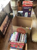 Box with assorted books packed vertically, showing mostly softcover titles with some colorful spines