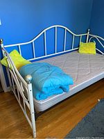 White metal daybed against blue wall with mattress, yellow throw pillows and blue comforter on top.