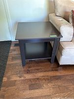 Pair of matching dark brown wooden square end tables with lower shelves, positioned beside a beige couch on hardwood floors.