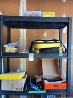 Full view of black shelving unit with yellow and black tool bags, boxes filled with tools and hardware parts.